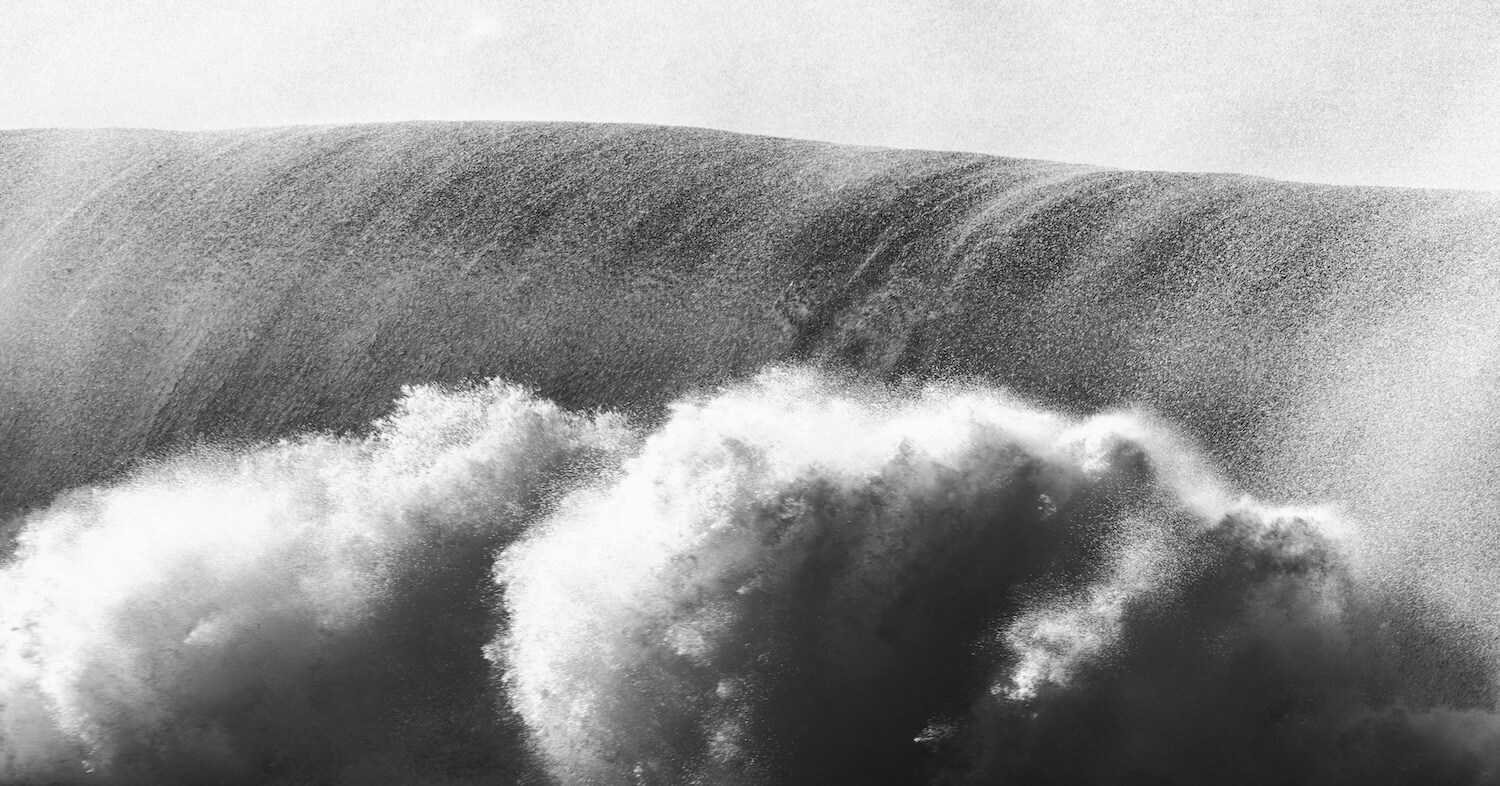 A huge wave crashes onto the shore in a black and white, grainy photograph