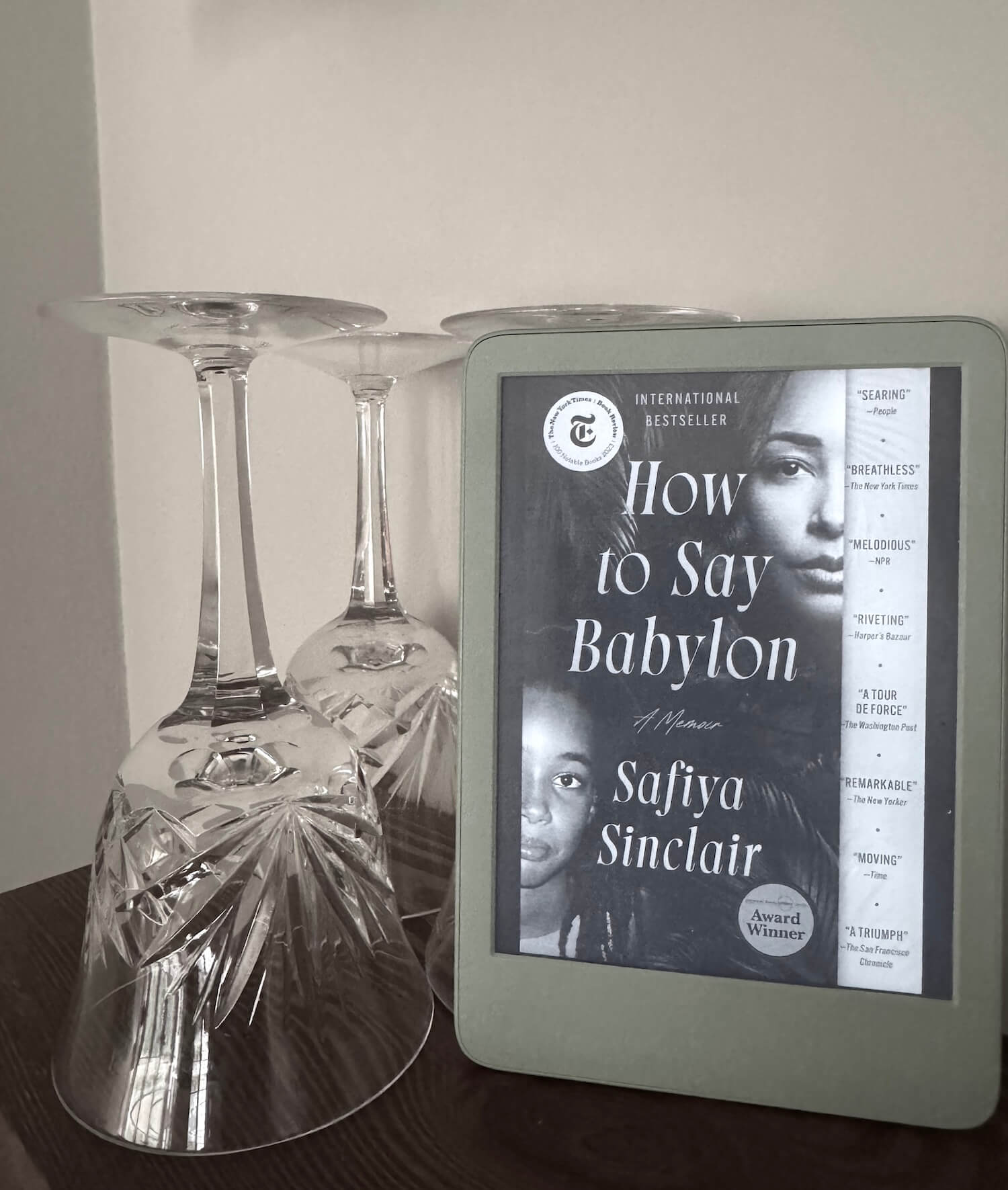 A kindle sets on a shelf next to vintage wine glasses.