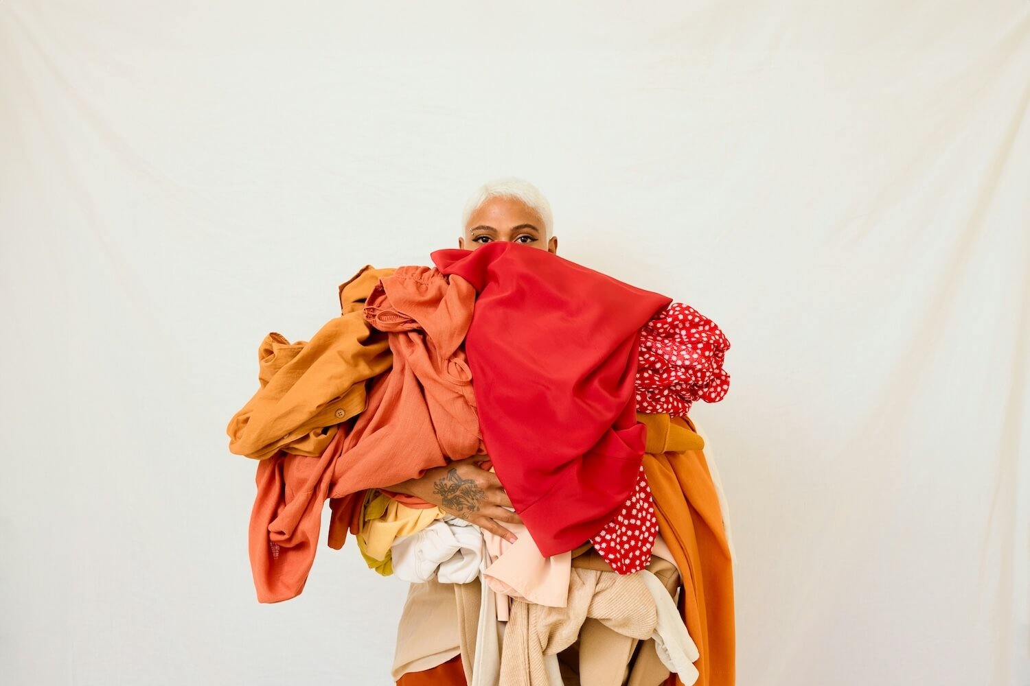 A woman holds a colorful overflowing array of clothes in her arms with only her eyes visible.